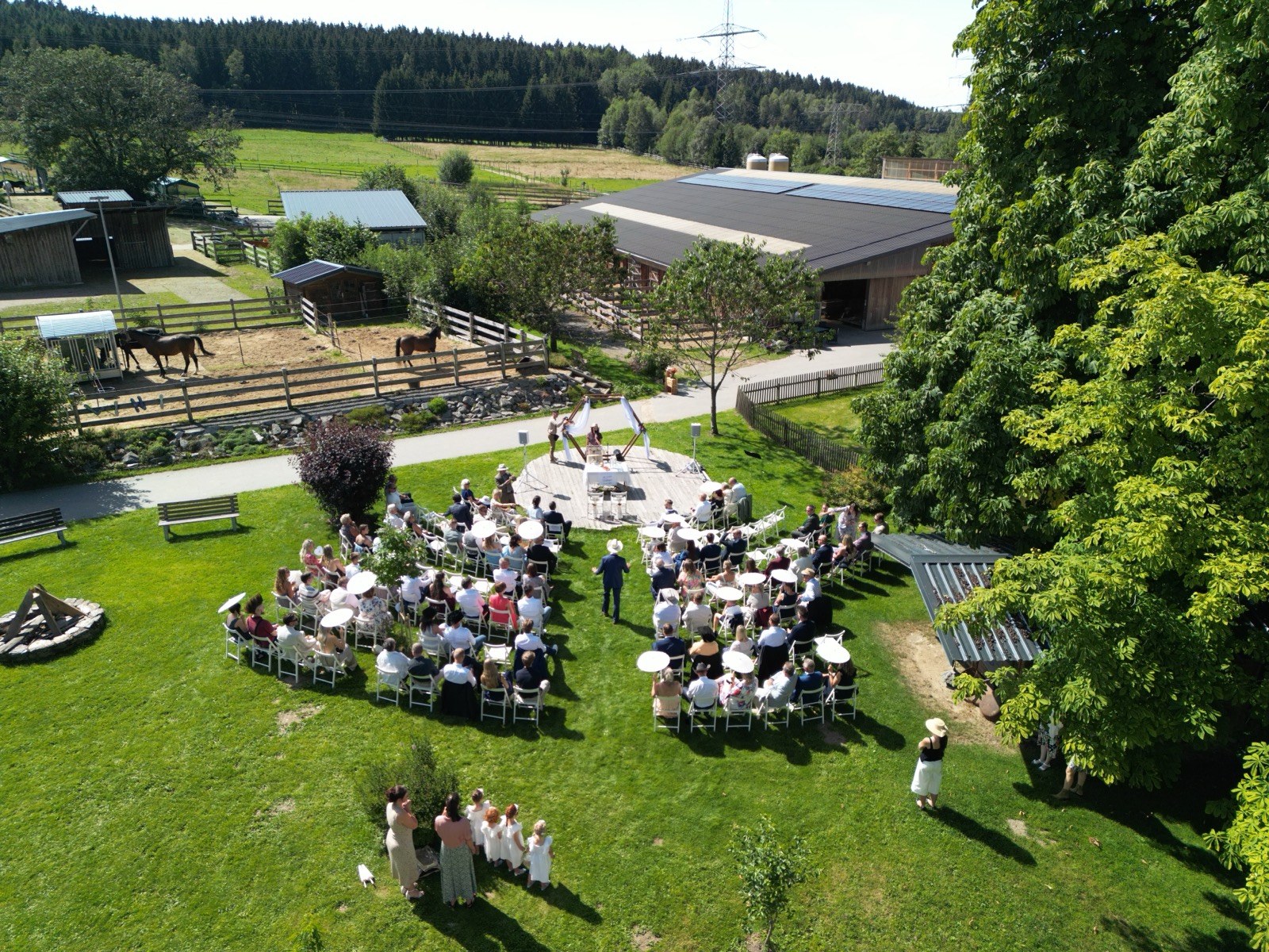 Freie Trauung auf der Wiese der Silver Rock Ranch aus der Luft: Gäste auf weißen Stühlen, Pferde im Paddock