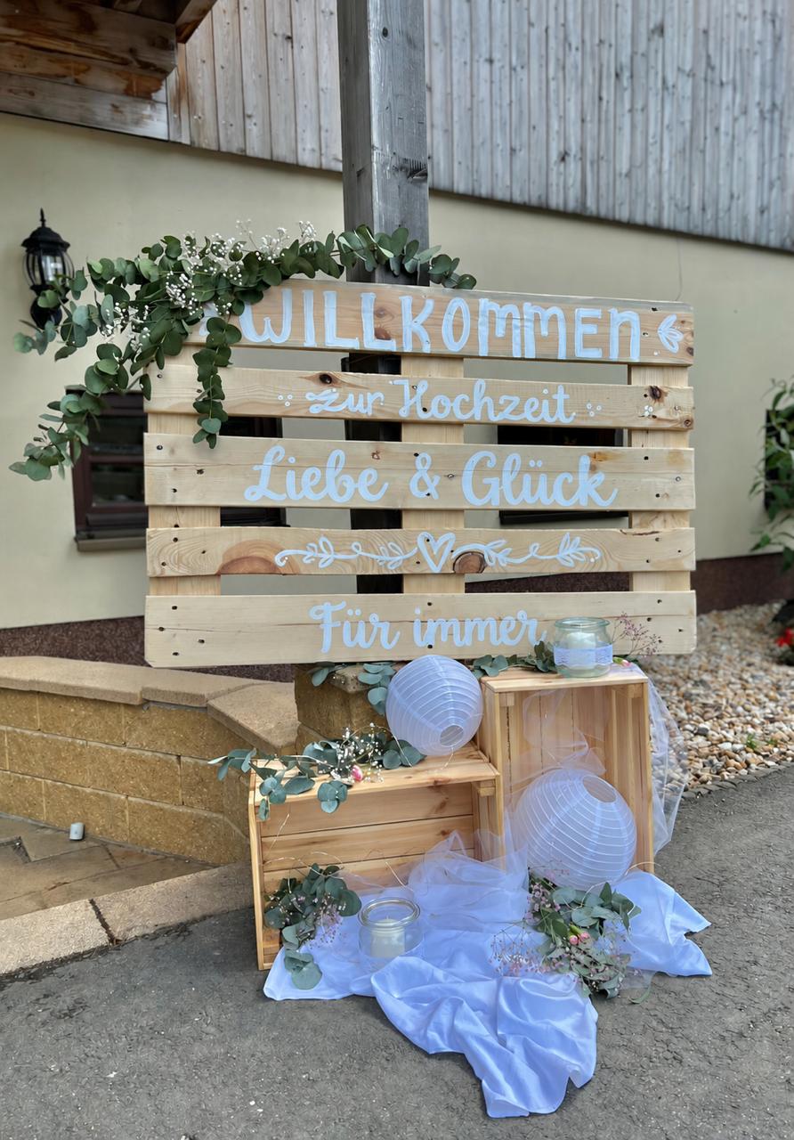 Willkommensschild zur Hochzeit aus Paletten mit Eukalyptus und Laternen